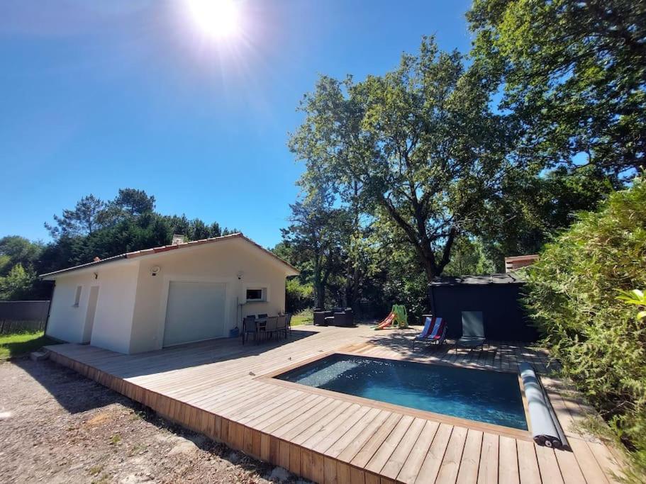 een achtertuin met een houten terras en een zwembad bij Maison au calme avec piscine in Carcans