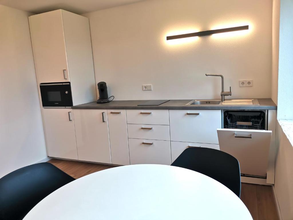 a kitchen with white cabinets and a sink and a table at Moderne Ferienwohnung Gartenblick in Amtzell