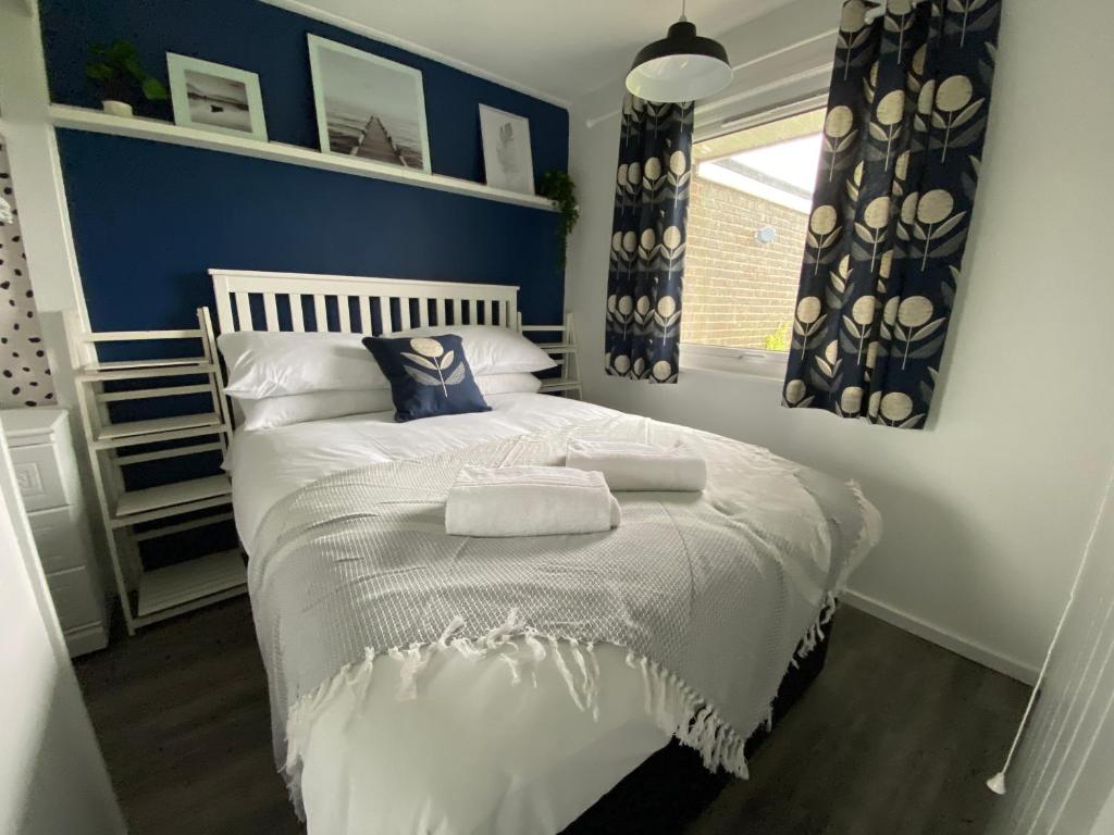 sypialnia z białym łóżkiem z niebieskimi ścianami i oknem w obiekcie East Coast Chalets 333 Sunny Corner at California Sands w mieście Great Yarmouth