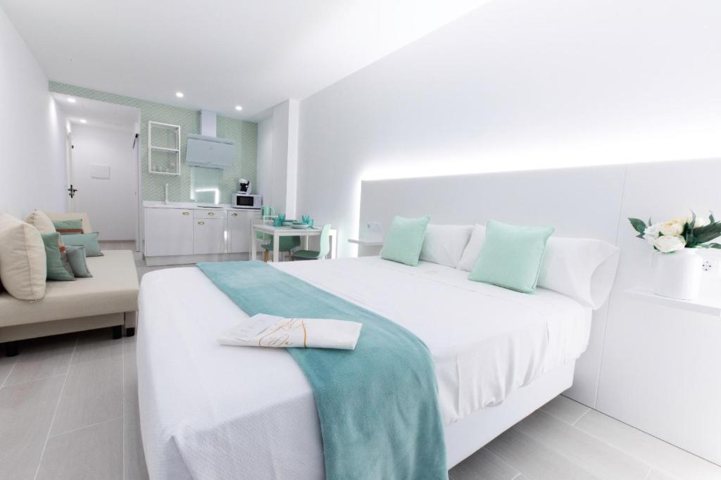 a white bedroom with a large white bed with a blue blanket at Apartamentos Ruta da Auga in Ribadumia