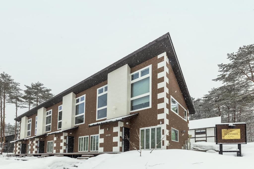a building in the snow with a sign in front of it at HOPETREE CoCo HAPPO TOWNS in Hakuba