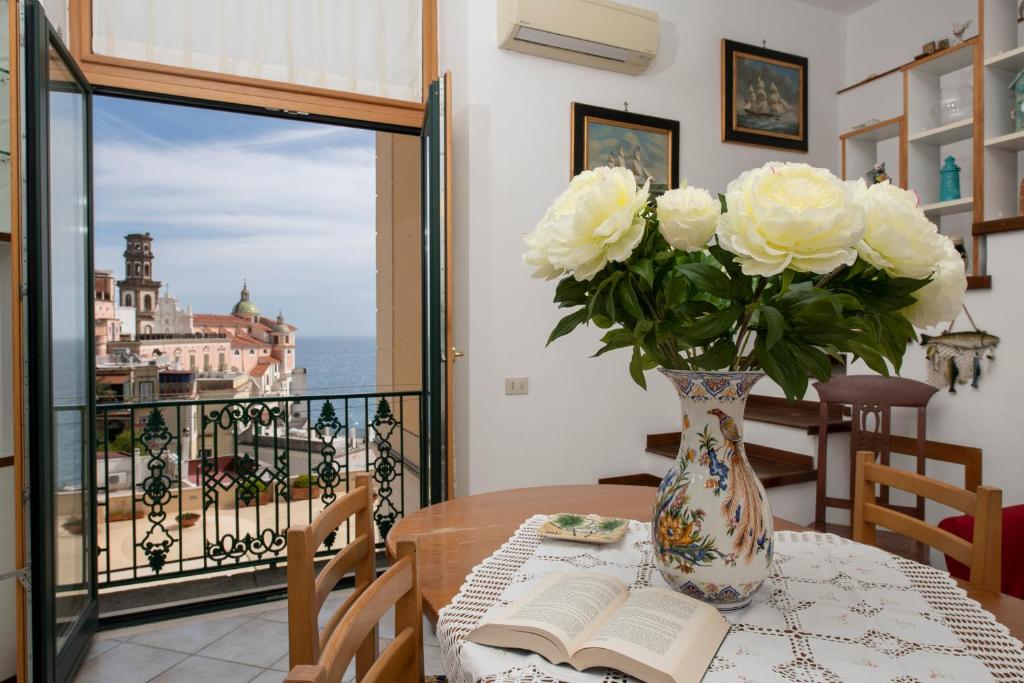 a vase with white roses on a table with a book at La casa di Carmela - Amalfi Coast in Atrani
