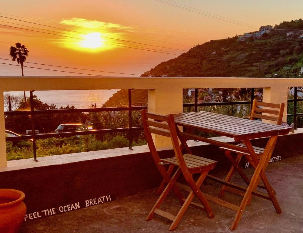 a wooden table and chairs on a balcony with the sunset at BnB BananaTree House in Arco da Calheta