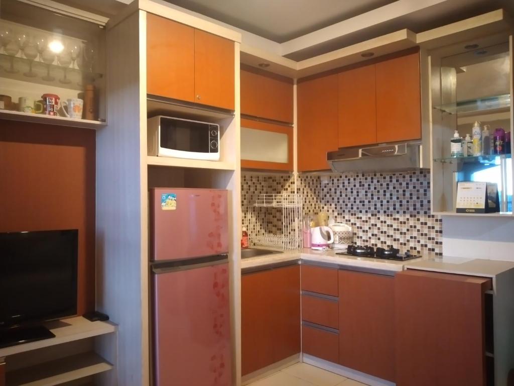 a kitchen with orange cabinets and a refrigerator at Tifolia Apartment Pulomas - Kelapa Gading in Jakarta