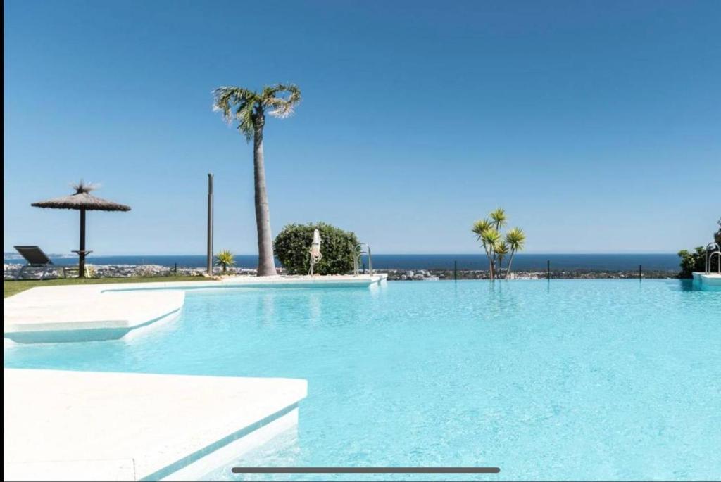 a large swimming pool with palm trees and the ocean at Panoramic Sea Views - Penthouse in Quartiers in Estepona