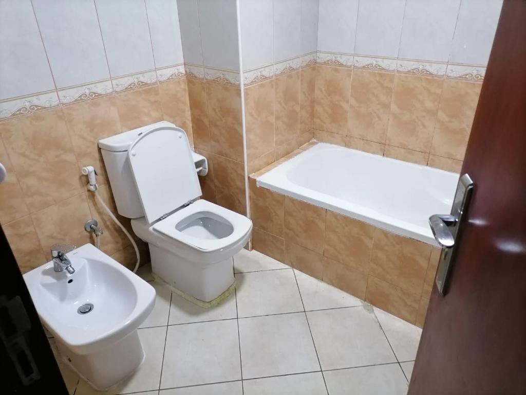 a bathroom with a toilet and a tub and a sink at MBZ - Comfortable Room in Unique Flat in Abu Dhabi