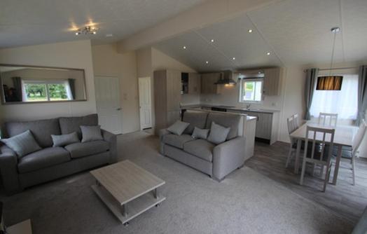 a living room with two couches and a table and a kitchen at Homeston Lodge in Drumlemble