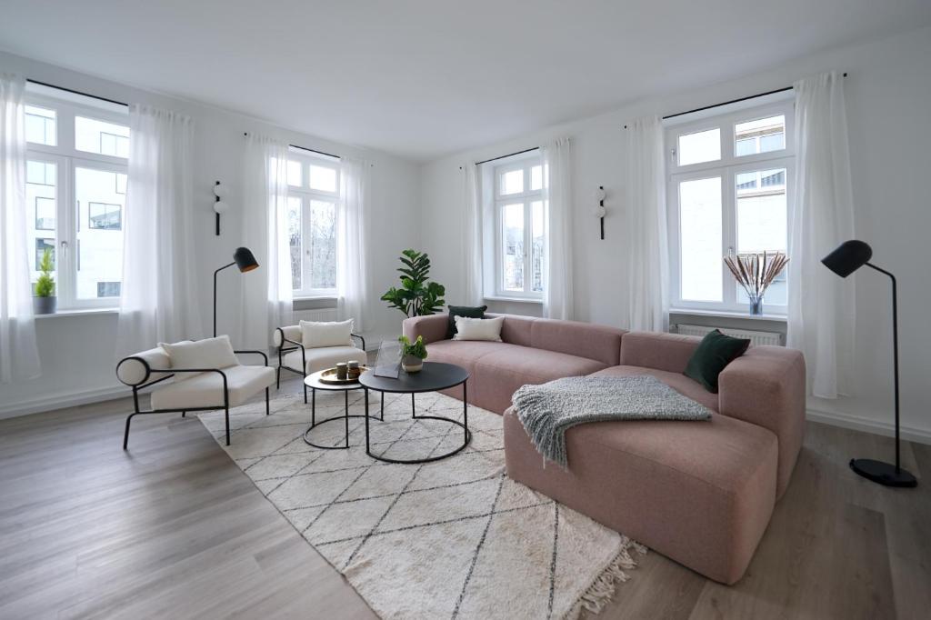 a living room with a pink couch and tables and windows at vonBehling Boutique Apartment - Gemeinsam leben am Puls der Innenstadt in Wiesbaden
