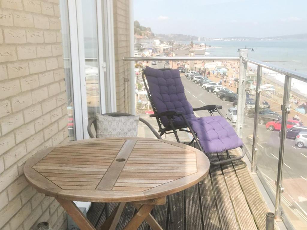 a wooden table and chairs on a balcony with a view of the ocean at Vue De Mer Ella in Shanklin