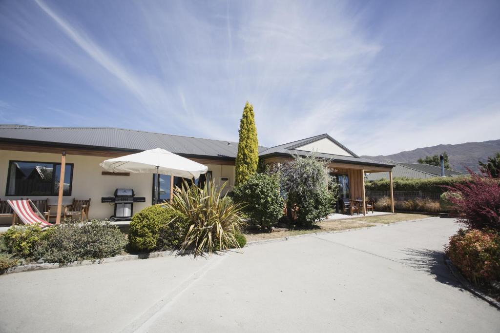 ein Haus mit einer Terrasse und einem Sonnenschirm in der Einfahrt in der Unterkunft Apollo Lodge and Apartment in Wanaka