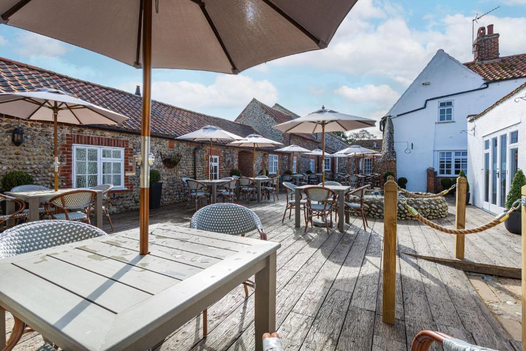 a patio with tables and chairs and umbrellas at The Manor Coastal Hotel & Inn, Blakeney - part of The Coaching Inn Group in Blakeney