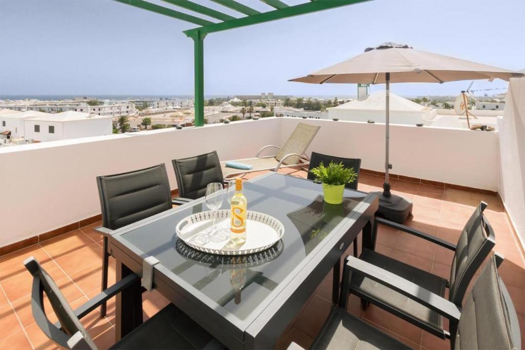 un tavolo da pranzo e sedie su un balcone con ombrellone di Apartamento OM con piscina y vistas al mar a Costa Teguise