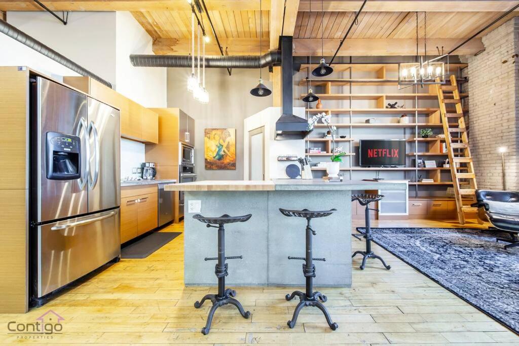 a kitchen with a refrigerator and a counter with bar stools at Historic JD Loft, Near ICE District, Rogers Place, UG Parking in Edmonton