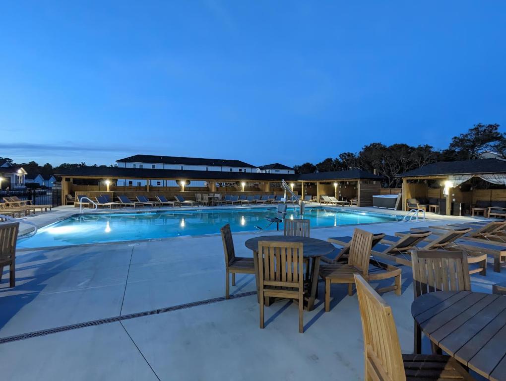 a resort pool with tables and chairs at night at Salty Kisses - Let The Beach Reconnect Your Souls in Corolla