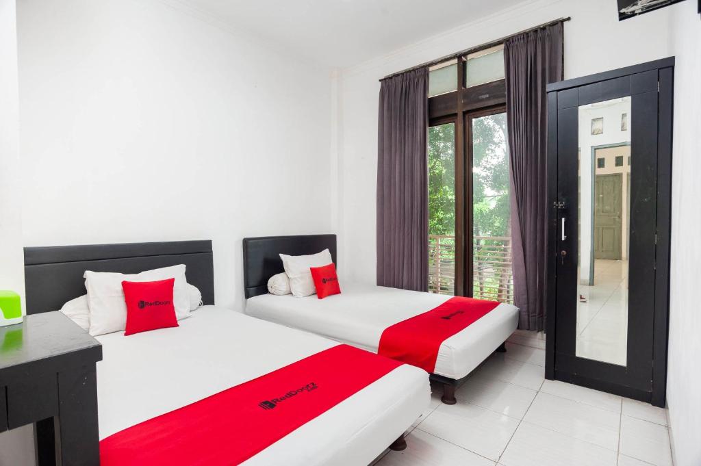Duas camas num quarto com almofadas vermelhas e brancas em RedDoorz Syariah near Grand Galaxy Park em Ceger