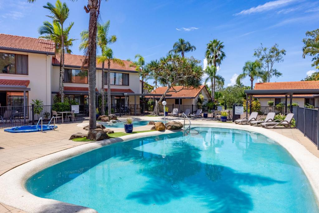a swimming pool at a resort with chairs and palm trees at Wolngarin Holiday Resort Noosa in Noosaville