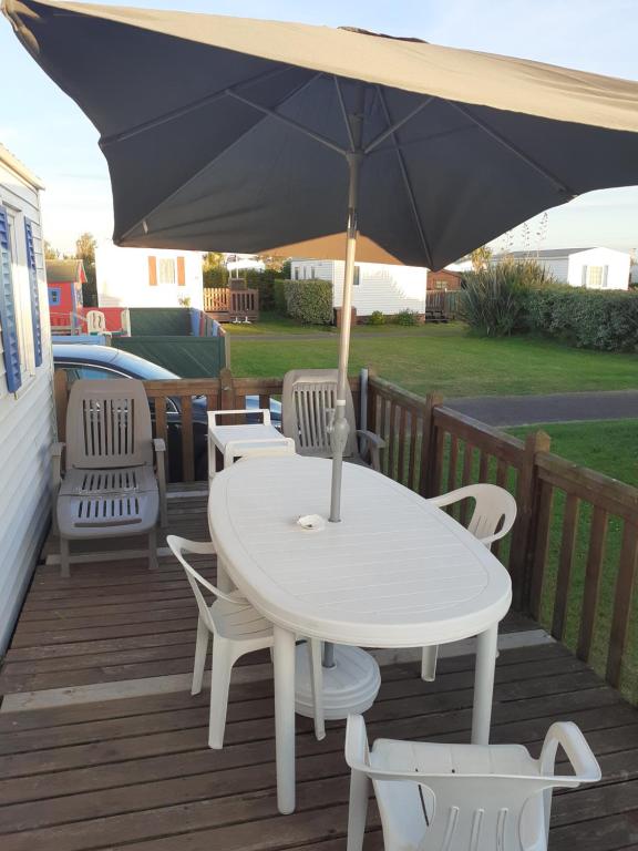 a white table and chairs with an umbrella on a deck at MH 4 personnes 5 étoiles plages du debarquement in Sainte-Mère-Église