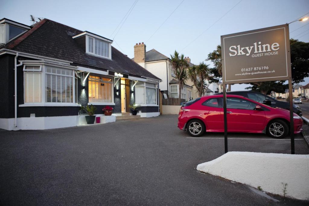 um carro vermelho estacionado em frente a uma placa em frente a uma casa em Skyline Guesthouse em Newquay