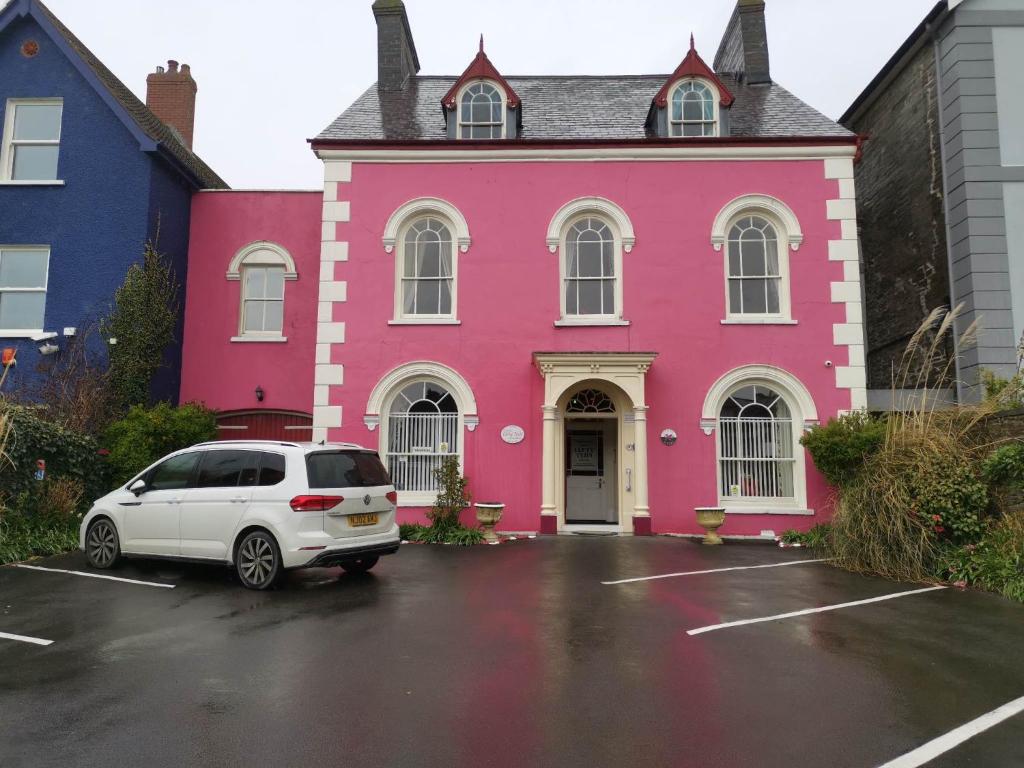 una casa rosa con un coche blanco aparcado en un aparcamiento en Llety Teifi Guest House, en Cardigan