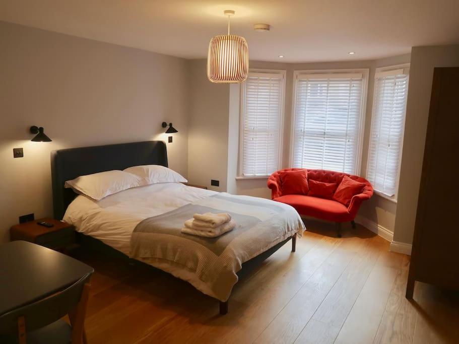 um quarto com uma cama e uma cadeira vermelha em Stylish Studio Apartment, ensuite, kitchenette em Twickenham