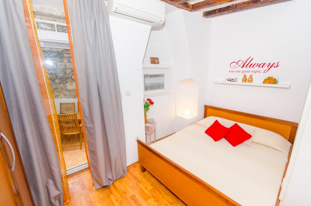 Habitación pequeña con cama con almohadas rojas en Studios Anna, en Rovinj