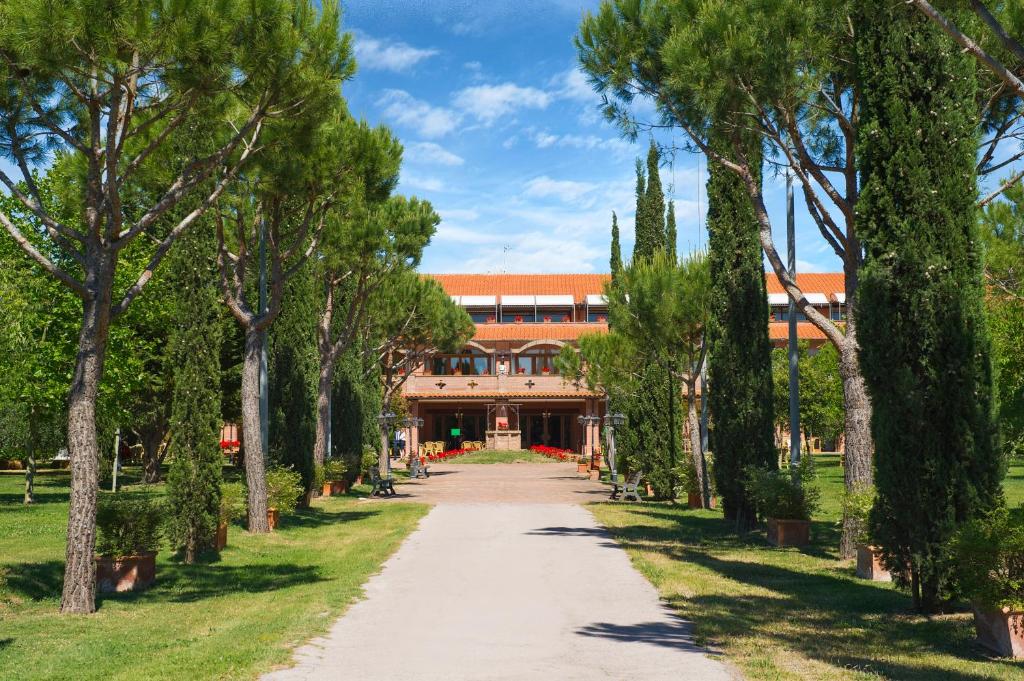 una passerella attraverso un parco alberato di fronte a un edificio di Fattoria La Principina Hotel & Congress a Principina Terra