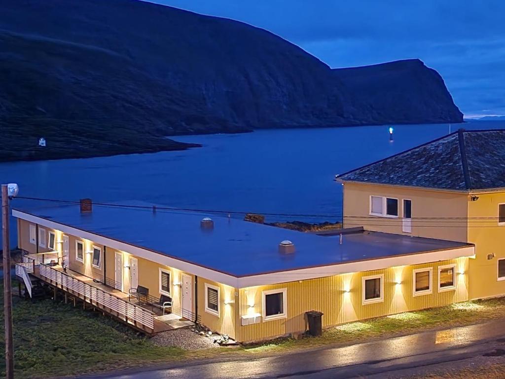 a house with lights on in front of a body of water at Kveldsol Apartments in Havøysund