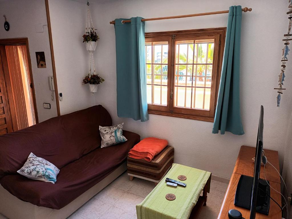 a living room with a brown couch and a window at Duplex junto a la playa in Arenales del Sol