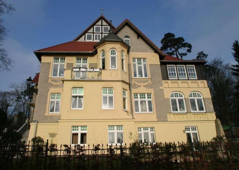une grande maison jaune avec des fenêtres blanches et une clôture dans l'établissement Villa Schulenburg in Putbus auf Rügen, à Putbus