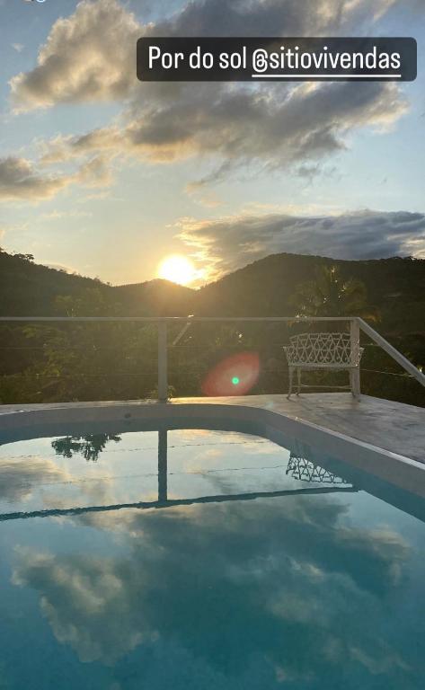 a bench sitting next to a swimming pool with the sunset at Sítio Vivendas in Itaipava