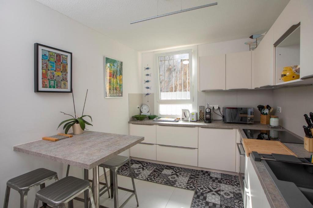 una cocina con armarios blancos y una mesa con taburetes en Appartement T3 Traversant Résidence Standing Garage et Piscine Extérieure GRATUITS en Sète