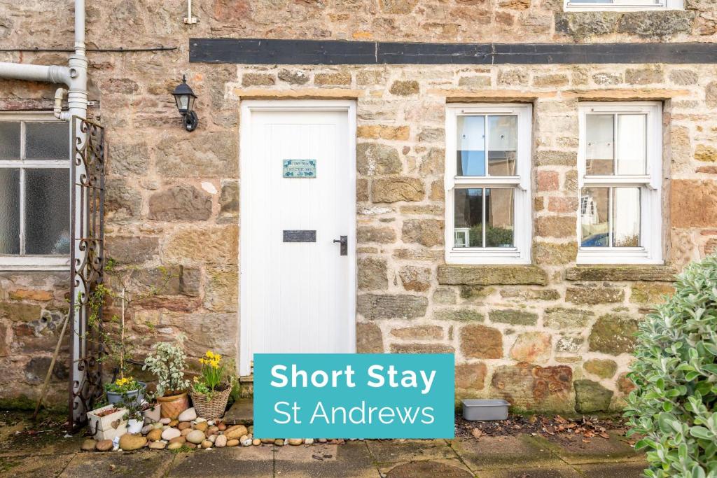 a stone house with a white door and windows at Stoney Creek Cottage - Cosy Cottage in the heart of Crail in Crail