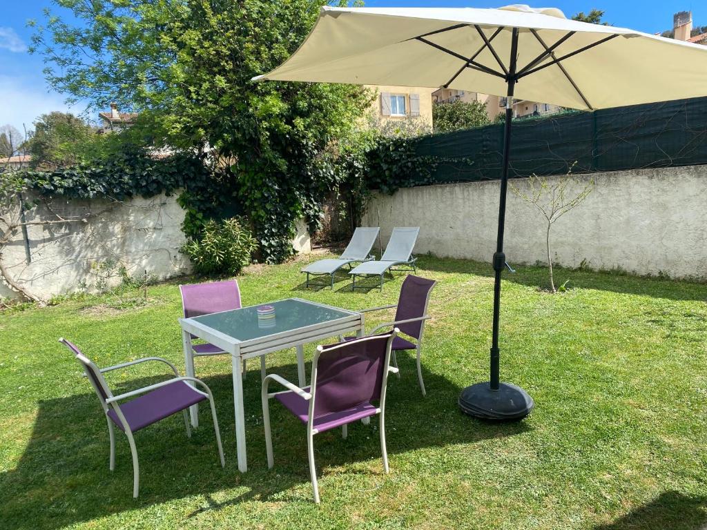 une table et des chaises avec un parasol dans l'herbe dans l'établissement Studio climatisé avec piscine et jardin, à Villeneuve-Loubet