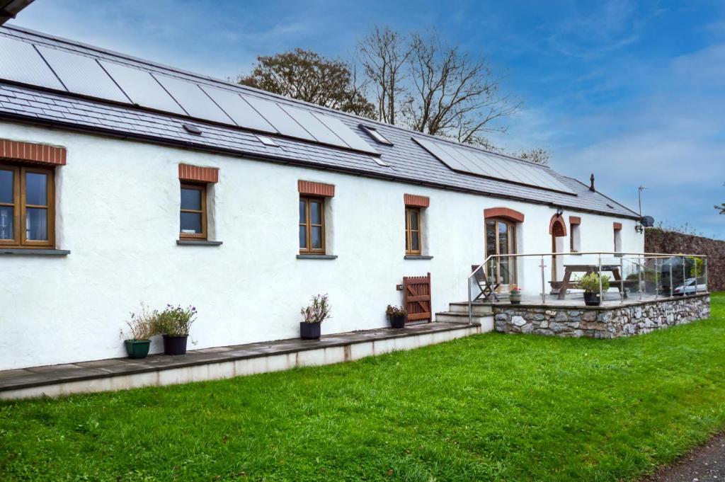 une maison blanche avec des panneaux solaires sur le toit dans l'établissement Orchard Cottage - Luxurious Barn Conversion - Beavers Hill, à Manorbier