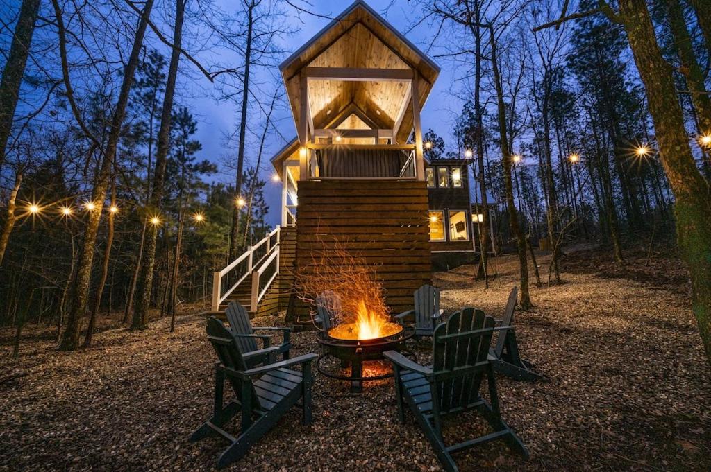 a fire pit with chairs and a house in the woods at Haven Hideaway, New Luxury Cabin w/ hot tub and fire pit in Broken Bow