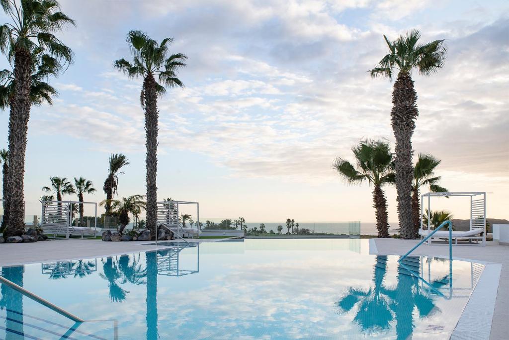 una piscina con palmeras y el océano en el fondo en THE CLUB - Accommodation - Dining - Events, en San Miguel de Abona