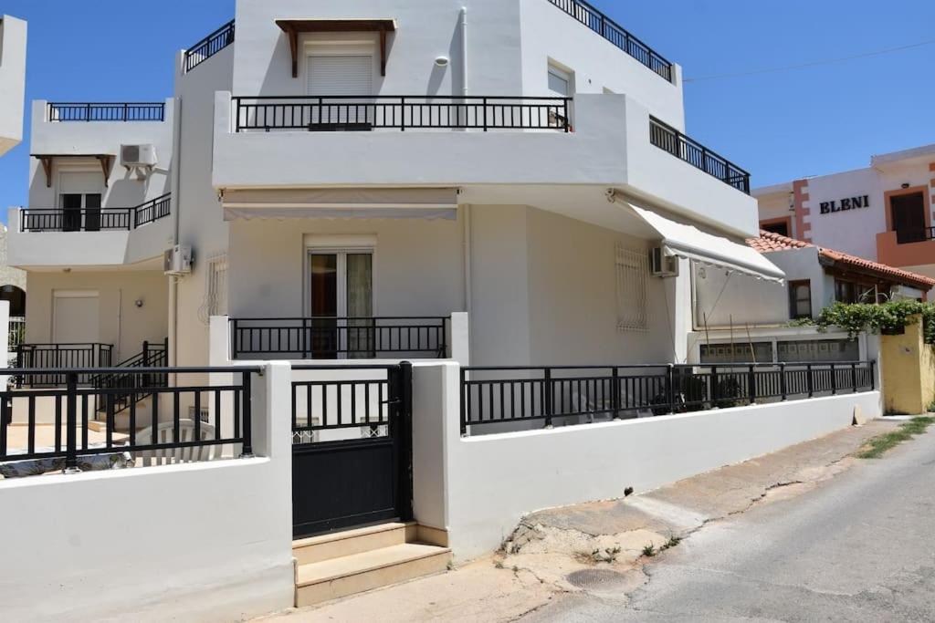 a white building with a black gate and balcony at Kouriton apartment is an ideal place to relax in Gouves