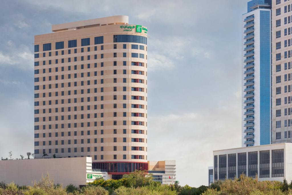a tall building with a green sign on top of it at Holiday Inn & Suites - Dubai Science Park, an IHG Hotel in Dubai
