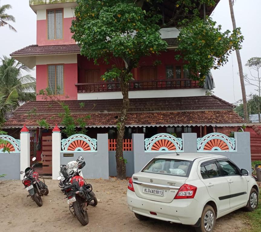 a white car parked in front of a house with two motorcycles at Wind Surf Beach House in Alleppey