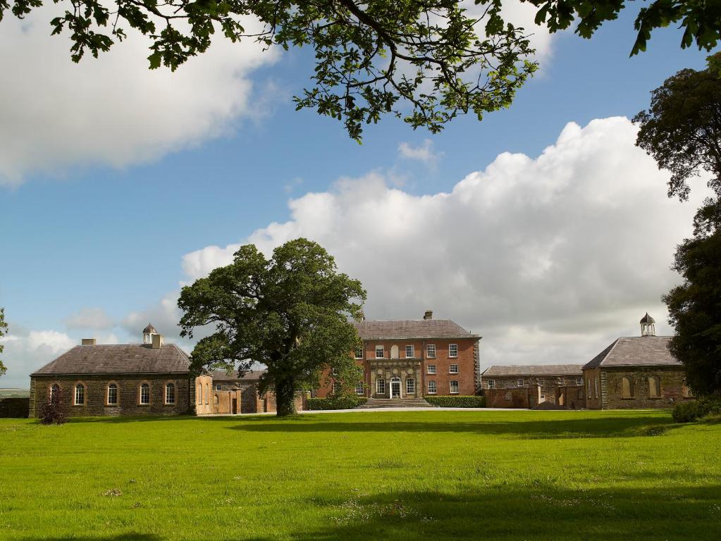 an old mansion with a tree in the middle of a field at The Courtyard Kilshannig in Fermoy