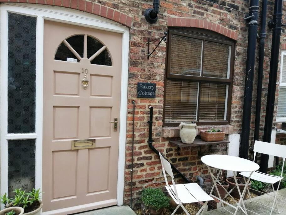 a pink door of a brick house with a table and chairs at Bakery Cottage Thirsk in Thirsk