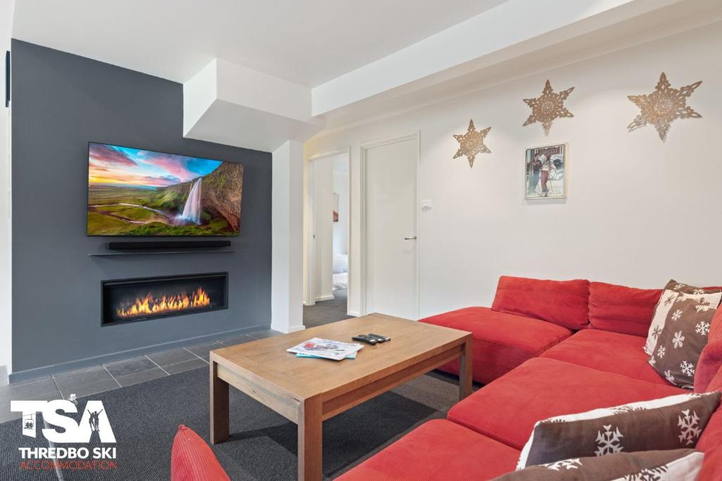 a living room with a red couch and a fireplace at Mowamba E5 in Thredbo