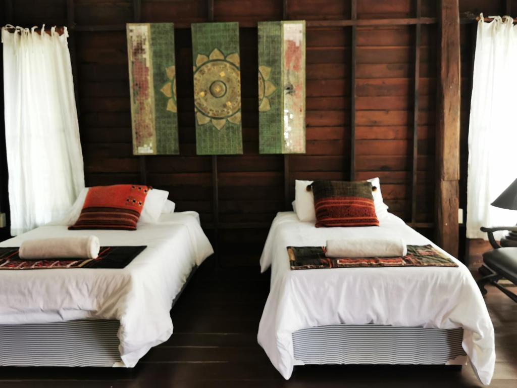 two beds in a room with wooden walls and windows at Jasmine Hills Lodge in Doi Saket