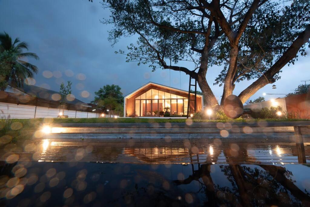 una casa di vetro con un albero di fronte di Nutnicha river house a Lam Phaya