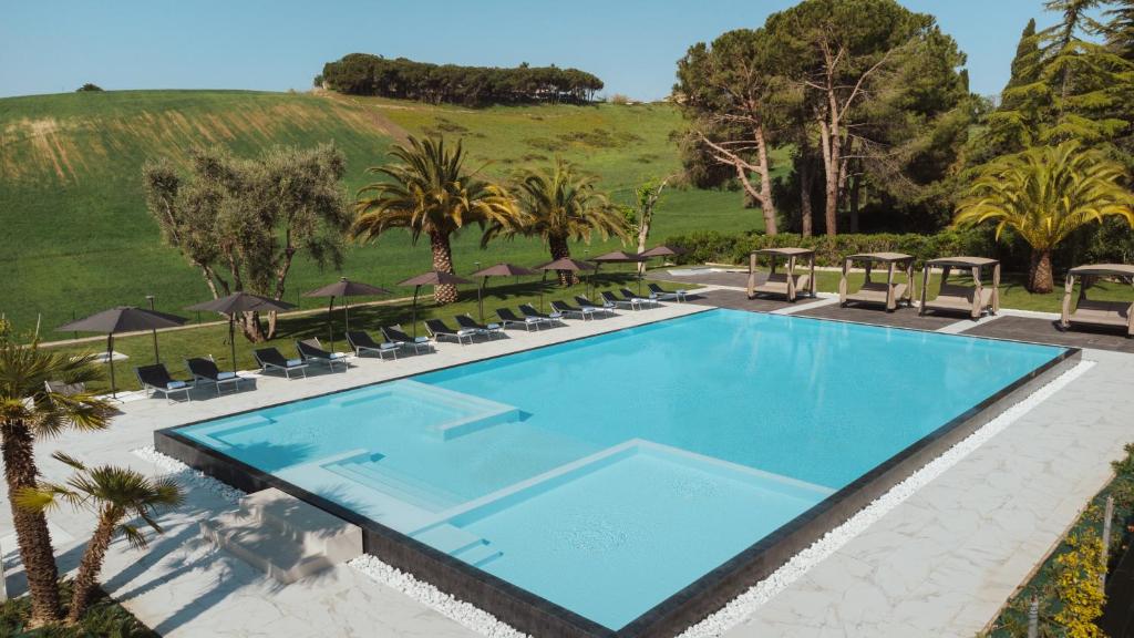 a swimming pool with chairs and trees and a hill at Pietra Bianca Hotel in Numana