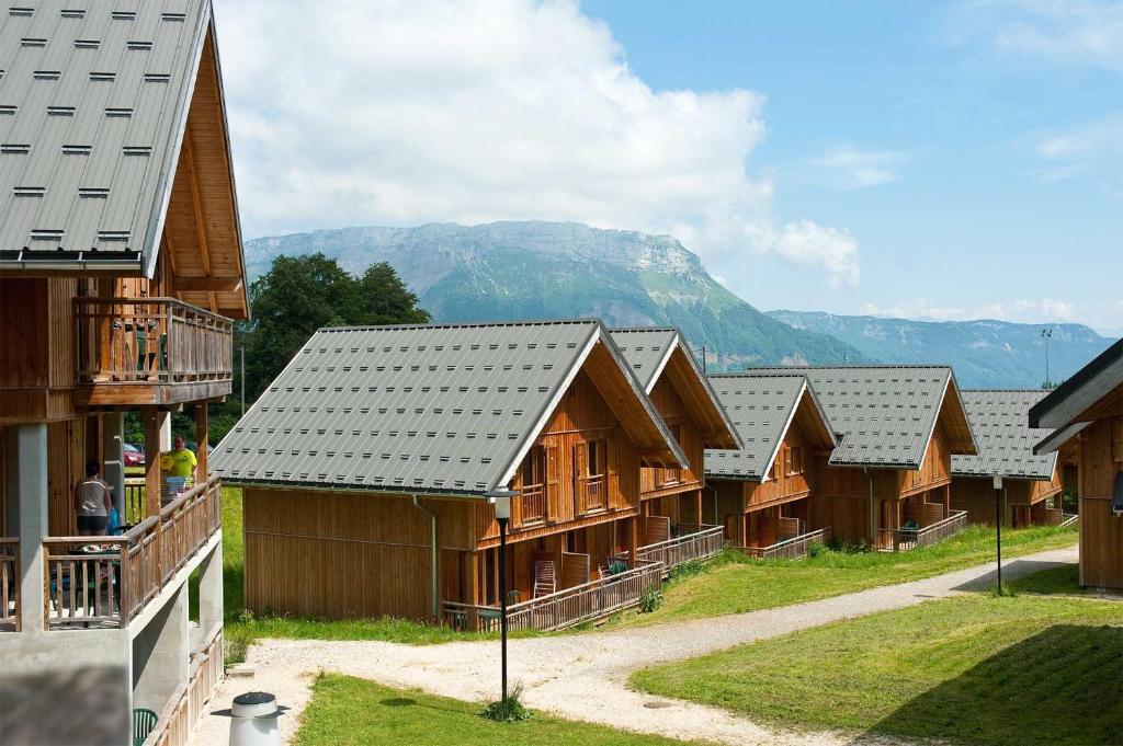 Une rangée de maisons en bois avec des montagnes en arrière-plan dans l'établissement Madame Vacances Les Chalets du Berger Premium***, à La Féclaz