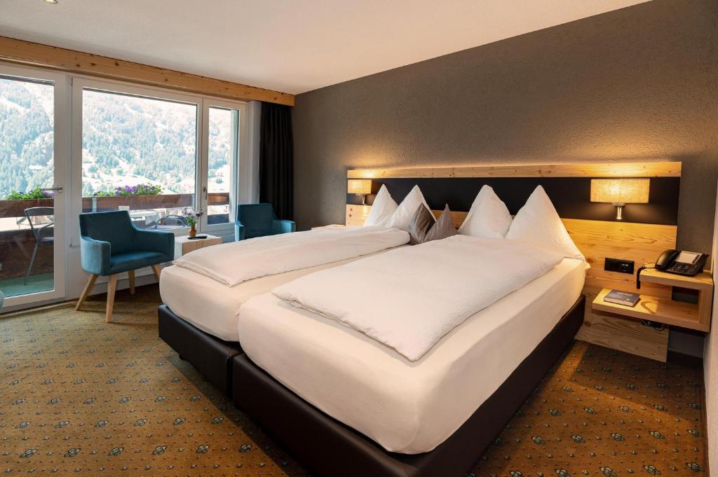 グリンデルワルトにあるホテル レストラン アルピナの大きなベッドと大きな窓が備わるホテルルームです。