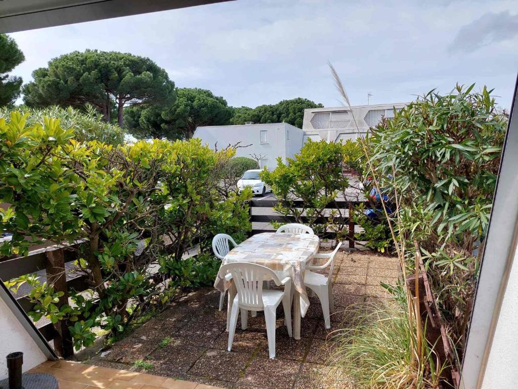 d'une terrasse avec une table, des chaises et des buissons. dans l'établissement Studio double cabine RDJ avec loggia et jardinet, parking privé, 5 pers - La Grande-Motte - FR-1-716-26, à La Grande Motte