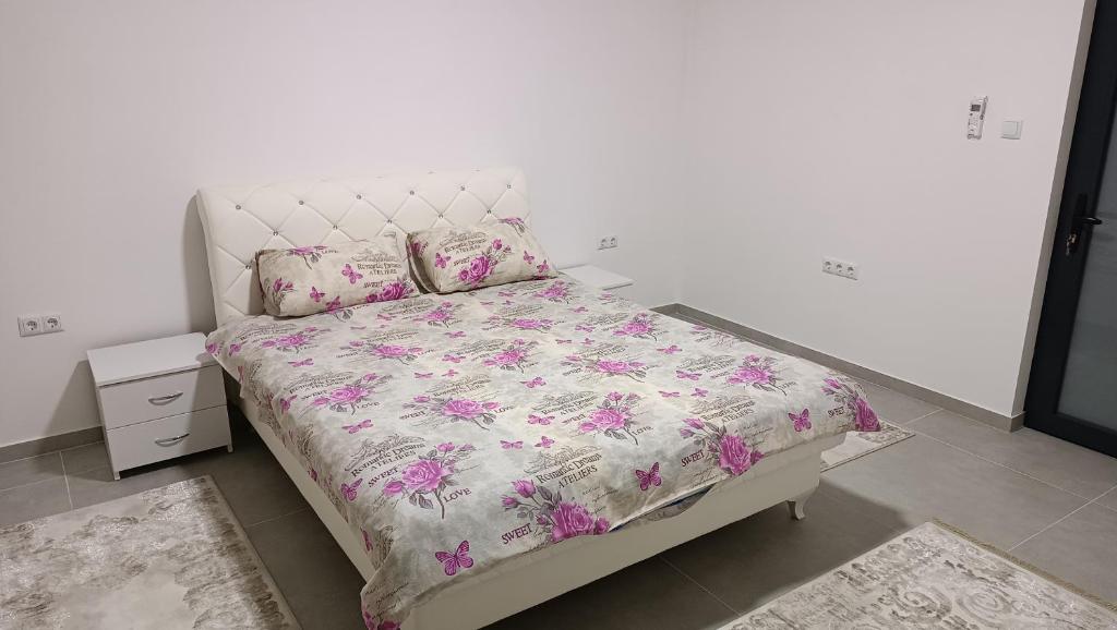 a bedroom with a bed with a floral bedspread and pillows at Grand Apartman in Živinice