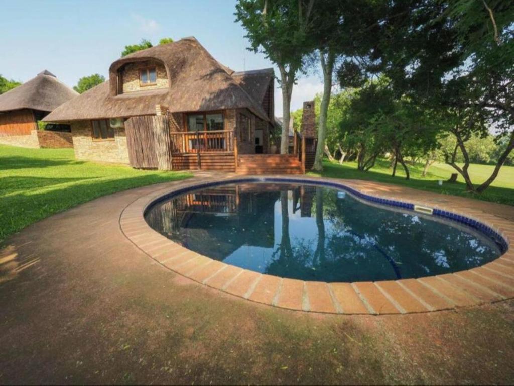 a swimming pool in front of a thatched house at Private Villa with Private Pool - Kruger Park Lodge in Hazyview